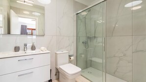 Een moderne badkamer met een douchecabine van glas, een witte wastafel met lades en een toilet.