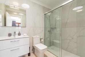 Ein modernes Badezimmer mit einer Duschkabine aus Glas, einem weißen Waschtisch mit Schubladen und einer Toilette.