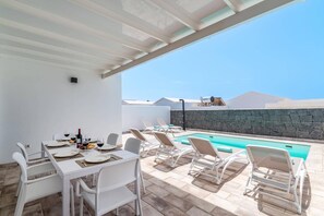Ein Essbereich im Freien mit Pool und Liegestühlen.