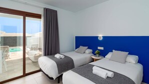 Een hotelkamer met twee bedden, een balkon met een zwembad en een blauwe accentmuur.