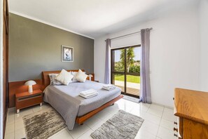 A bedroom with a bed, bedside tables, a nightstand, a picture on the wall, and a view of the outdoors through a sliding door. - Villa Casa Mafalda by Villa Plus (Carvoeiro)