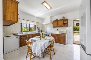 A kitchen with wooden cabinets, a dining table with chairs, and a view of the outdoors. - Villa Casa Mafalda by Villa Plus (Carvoeiro)