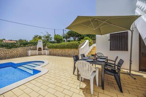 A pool area with a stone wall, a barbecue, and a dining setup with chairs and a table. - Villa Casa Mafalda by Villa Plus (Carvoeiro)
