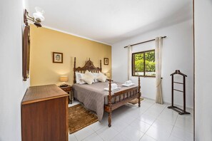 A bedroom with a wooden bed, a nightstand, a lamp, a window with curtains, and a wooden ladder. - Villa Casa Mafalda by Villa Plus (Carvoeiro)