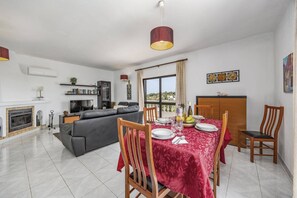 A modern living room with a fireplace, a dining area with a red tablecloth, and a view of the outdoors. - Villa Casa Mafalda by Villa Plus (Carvoeiro)