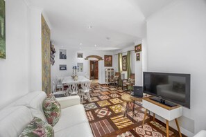 Ein Wohnzimmer mit Fernseher, weißem Sofa, einem gemusterten Boden und einem Essbereich mit Tisch und Stühlen.
