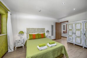 Une chambre à coucher avec une couvre-lit verte, une tête de lit ornée d’un motif décoratif, deux lampes de chevet et une armoire au design classique.