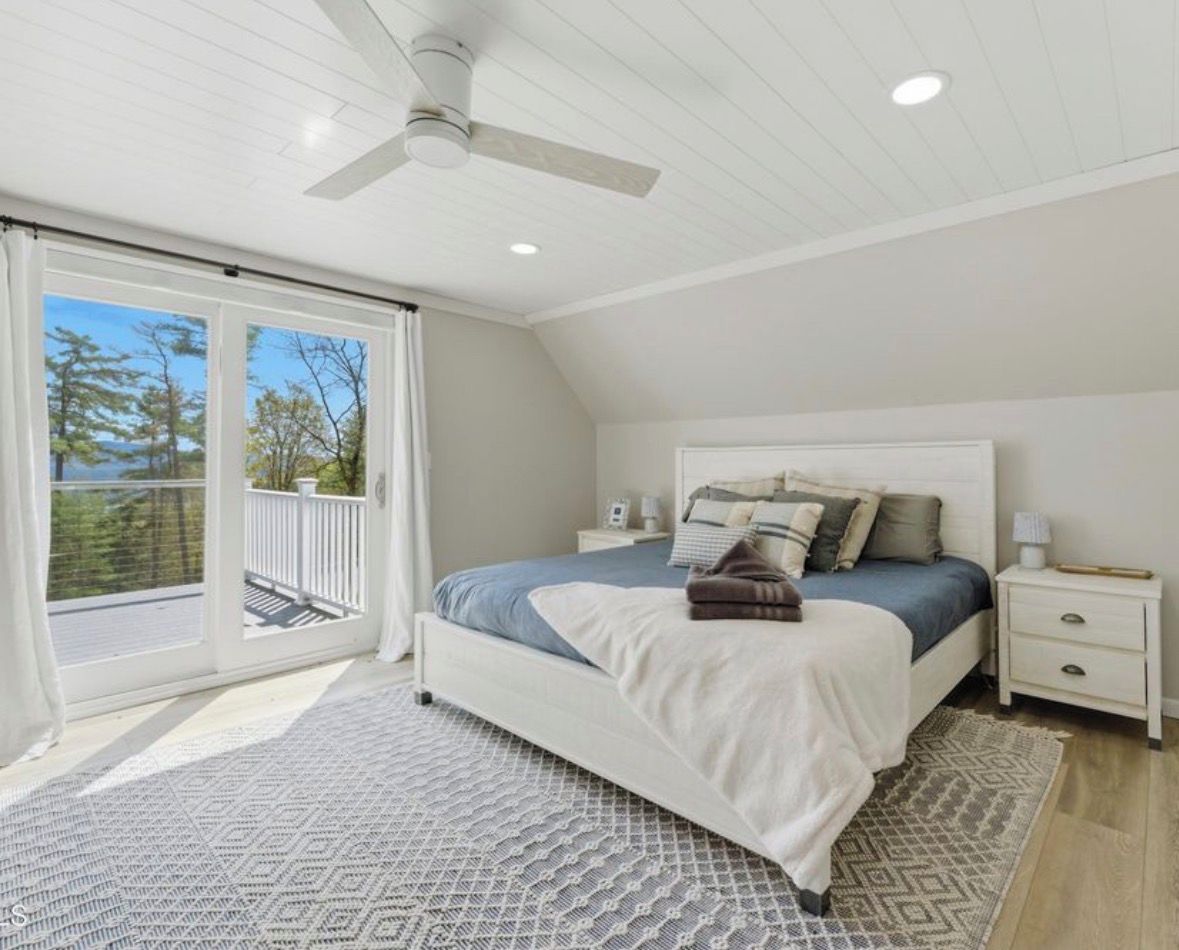Une chambre avec un lit, des tables de chevet, un ventilateur de plafond et une vue sur une terrasse extérieure, accessible par une porte-fenêtre coulissante.