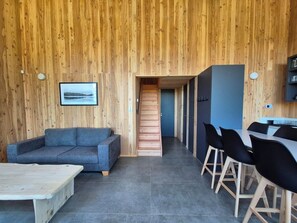 A modern interior with a wooden wall, a grey sofa, a dining table with chairs, and a staircase leading to another room. - Hestia en Dachas Patagonia (San Carlos de Bariloche)