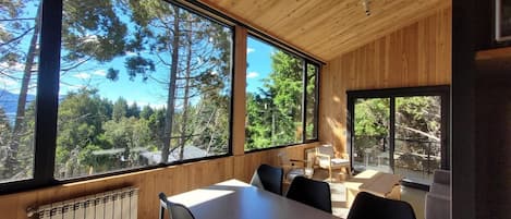 Habitación con un ventanal que ofrece vistas a árboles y montañas. Hay una mesa con sillas y un radiador debajo de la ventana.
