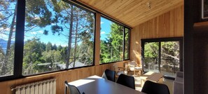 A room with a large window offering a view of trees and mountains. There is a table with chairs and a radiator below the window.
