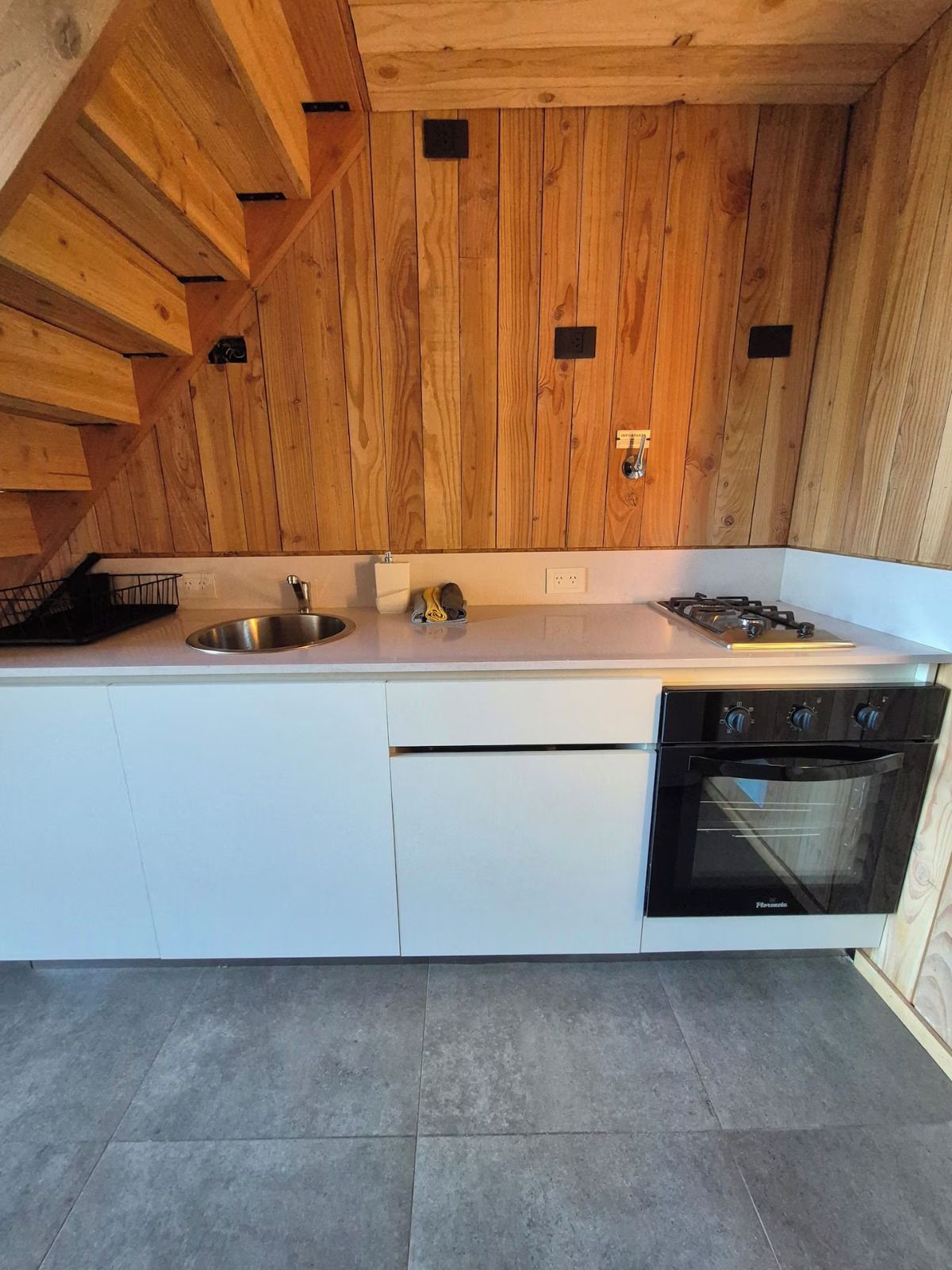 A kitchen with wooden walls, a stainless steel sink, a gas stove, and a built-in oven.