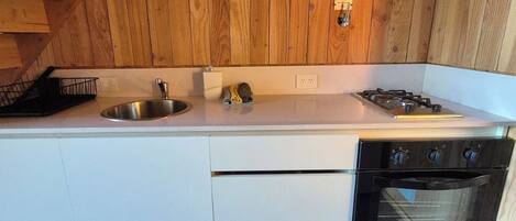 A kitchen with wooden walls, a stainless steel sink, a gas stove, and a built-in oven.