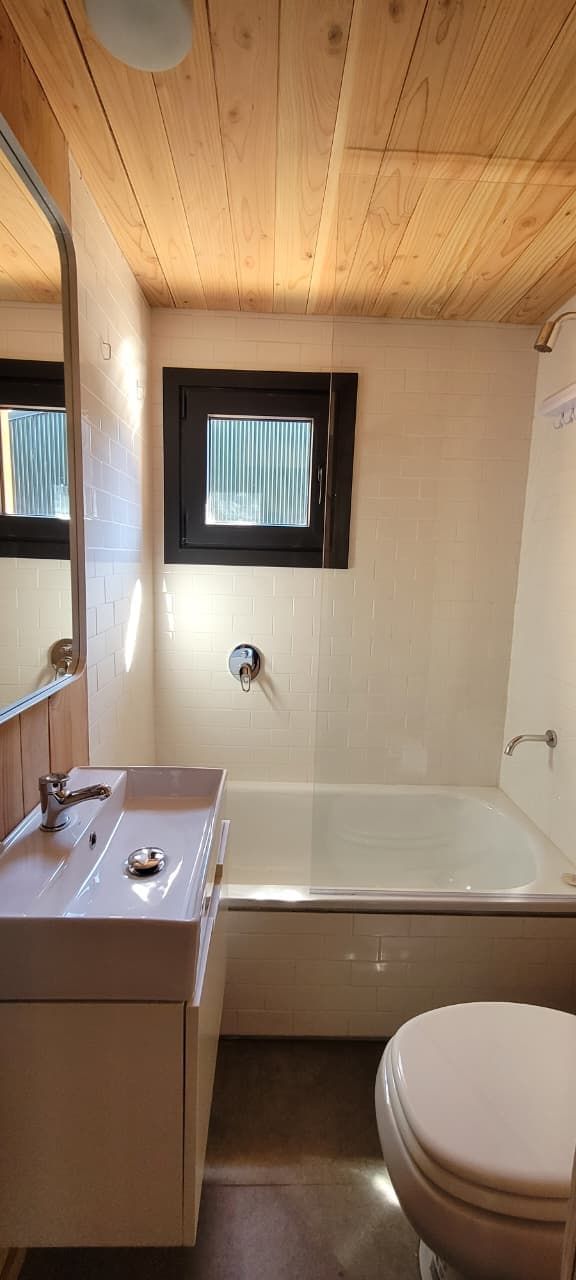 A bathroom with a wooden ceiling, a window, a bathtub, a toilet, and a sink.