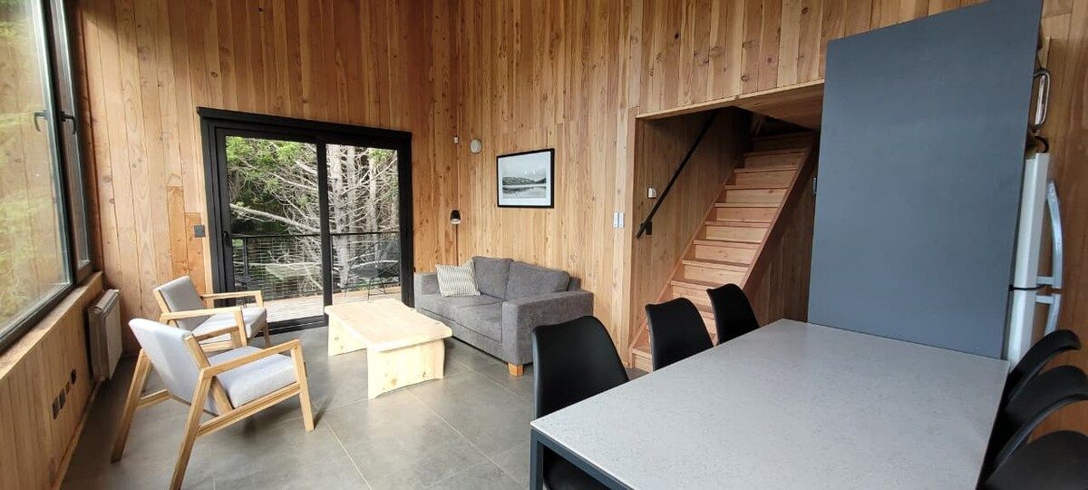 A modern interior with a wooden wall, a sofa, a dining table, and a staircase.