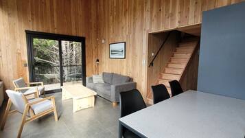 A modern interior with a wooden wall, a sofa, a dining table, and a staircase.