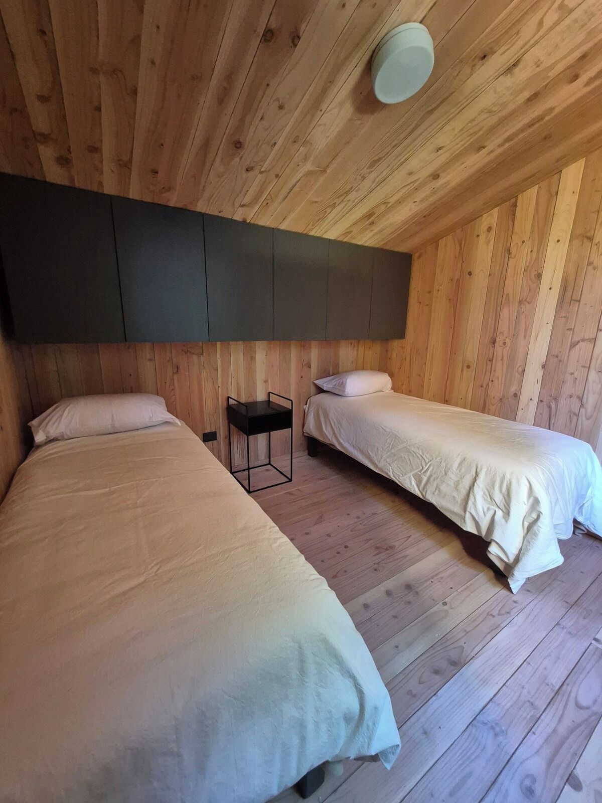A room with two beds, a small table, and a ceiling light fixture.