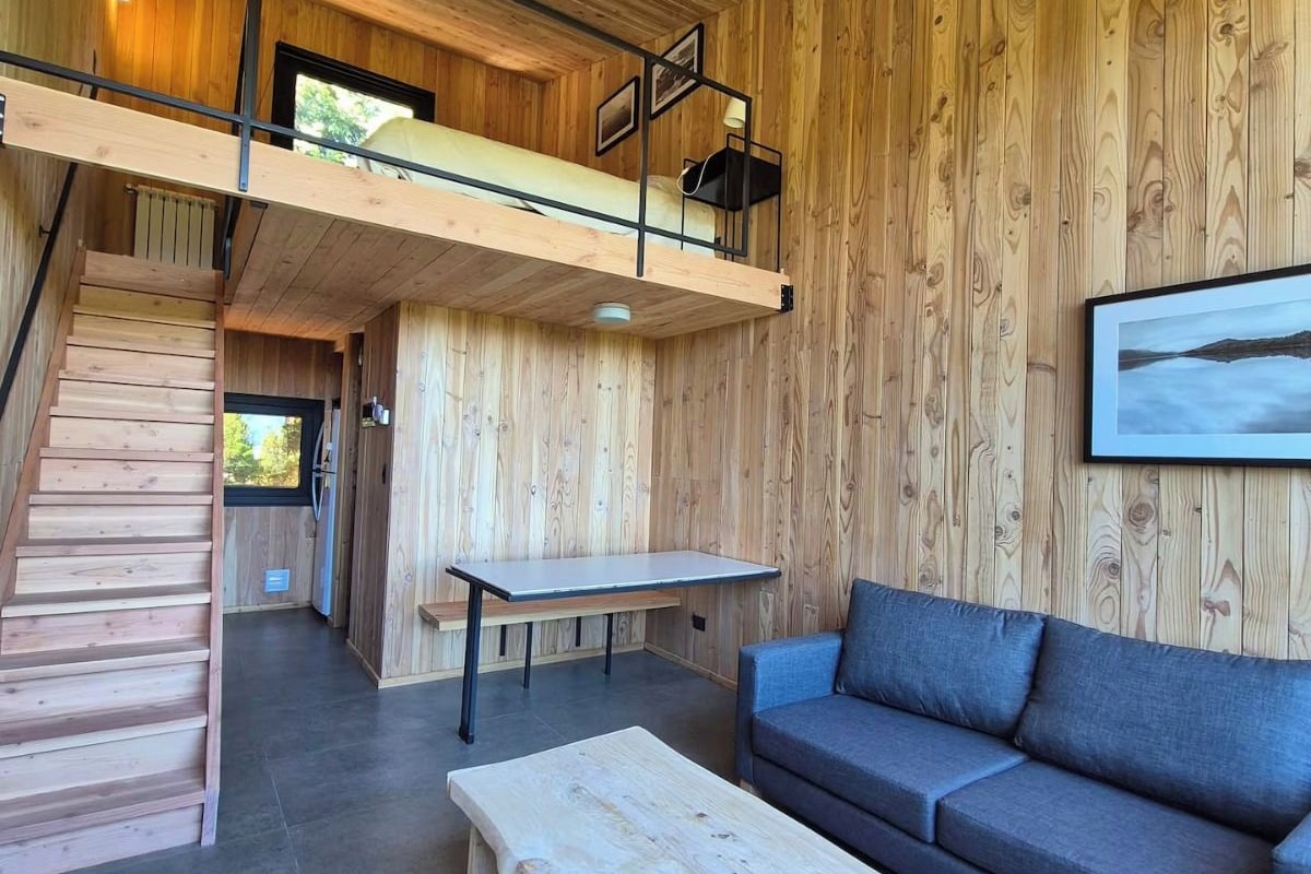 A modern interior with a loft bedroom, a dining area, and a seating area with a sofa and coffee table.