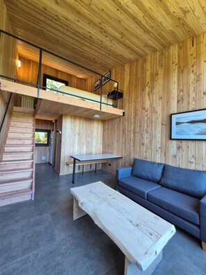 Un interior moderno con un dormitorio en loft, un comedor y una zona de estar con sofá y mesa de centro.