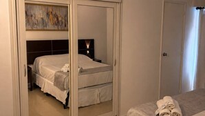 A bedroom with a bed, a wardrobe with a mirror, and a nightstand with a lamp. - Hotel Aquarium (Punta del Este)
