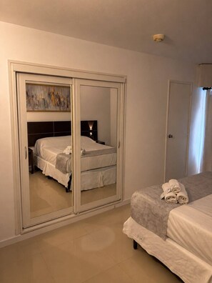 A bedroom with a bed, a wardrobe with a mirror, and a nightstand with a lamp. - Hotel Aquarium (Punta del Este)