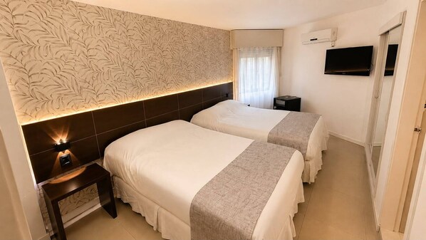A hotel room with two beds, a nightstand, a TV, and a window with curtains. - Hotel Aquarium (Punta del Este)