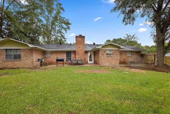 A two-story brick house with a front yard, a chimney, and a covered patio area.