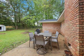 An outdoor patio with a brick wall, a table with chairs, and a grill.