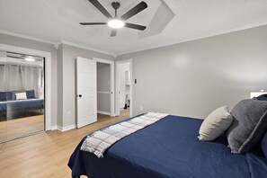 A bedroom with a bed, a ceiling fan, and a sliding glass door leading to a bathroom.