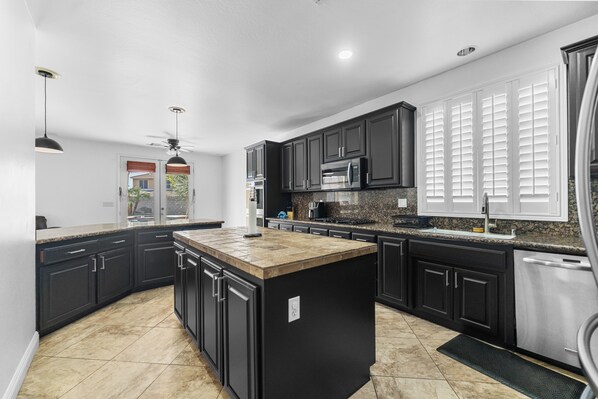 A modern kitchen with dark cabinetry, a central island, and a built-in microwave. - Lovely 5-bedroom 3 Full Bathroom House In Charming Southwest Bakersfield (Bakersfield)