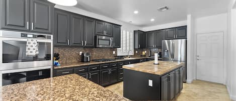 Una cocina moderna con encimeras de granito, electrodomésticos de acero inoxidable y muebles oscuros.