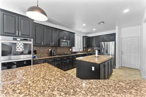 Moderni keittiö, jossa on graniittitasot, ruostumattomasta teräksestä valmistetut kodinkoneet ja tummat kaapistot.