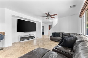 A modern living room with a flat-screen TV, leather sofa, and a ceiling fan. - Lovely 5-bedroom 3 Full Bathroom House In Charming Southwest Bakersfield (Bakersfield)