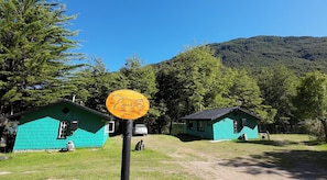 Two small green cabins with a sign in front, surrounded by trees and a mountain in the background. - Esparza lodge (Los Lagos)