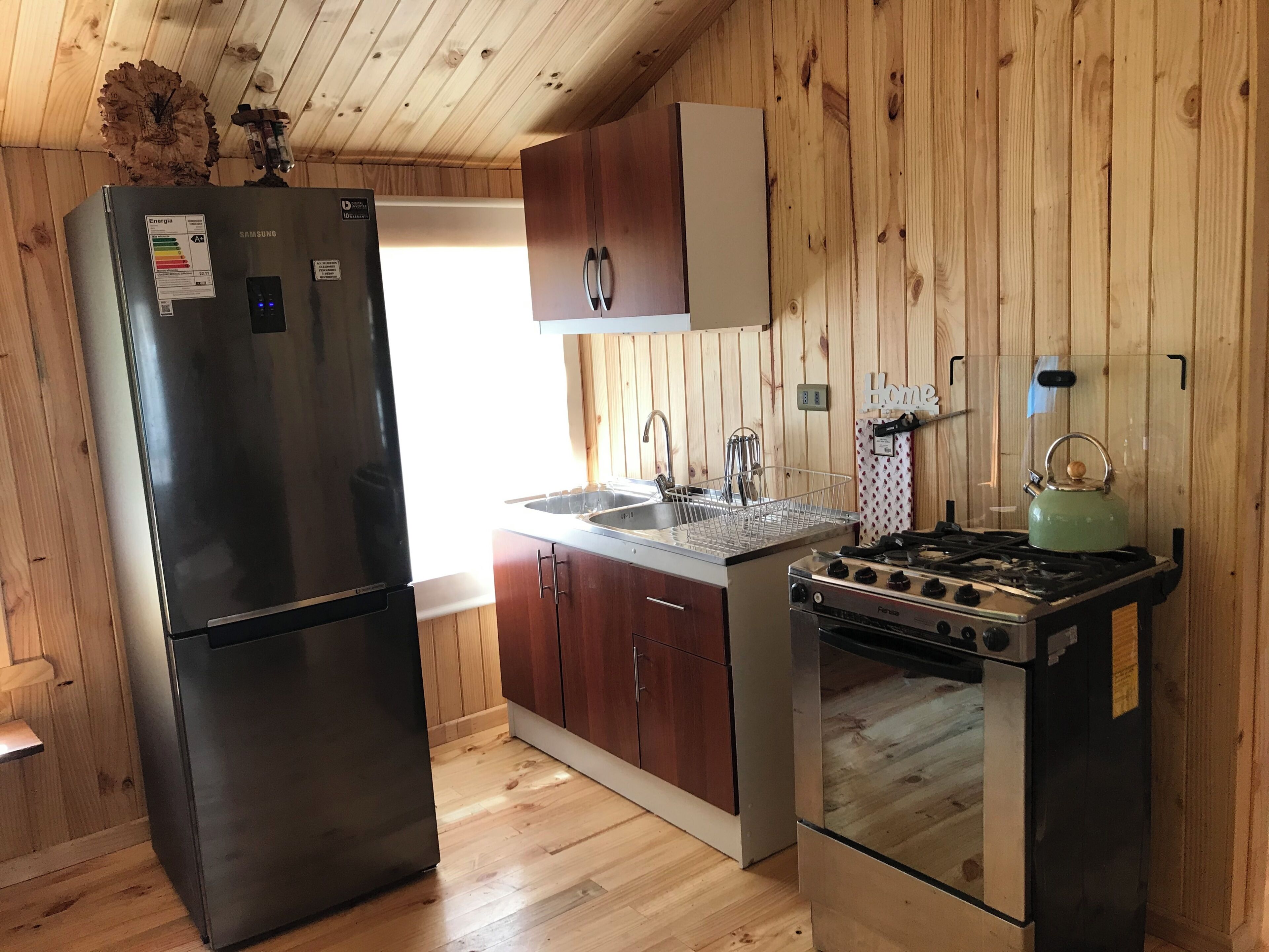 Una cocina compacta con refrigerador de acero inoxidable, gabinetes de madera, estufa a gas y un lavamanos.