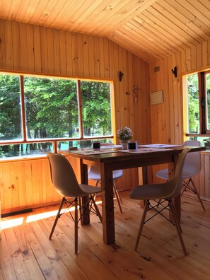 A wooden interior with a table and chairs, large windows, and a view of trees. - Esparza lodge (Los Lagos)