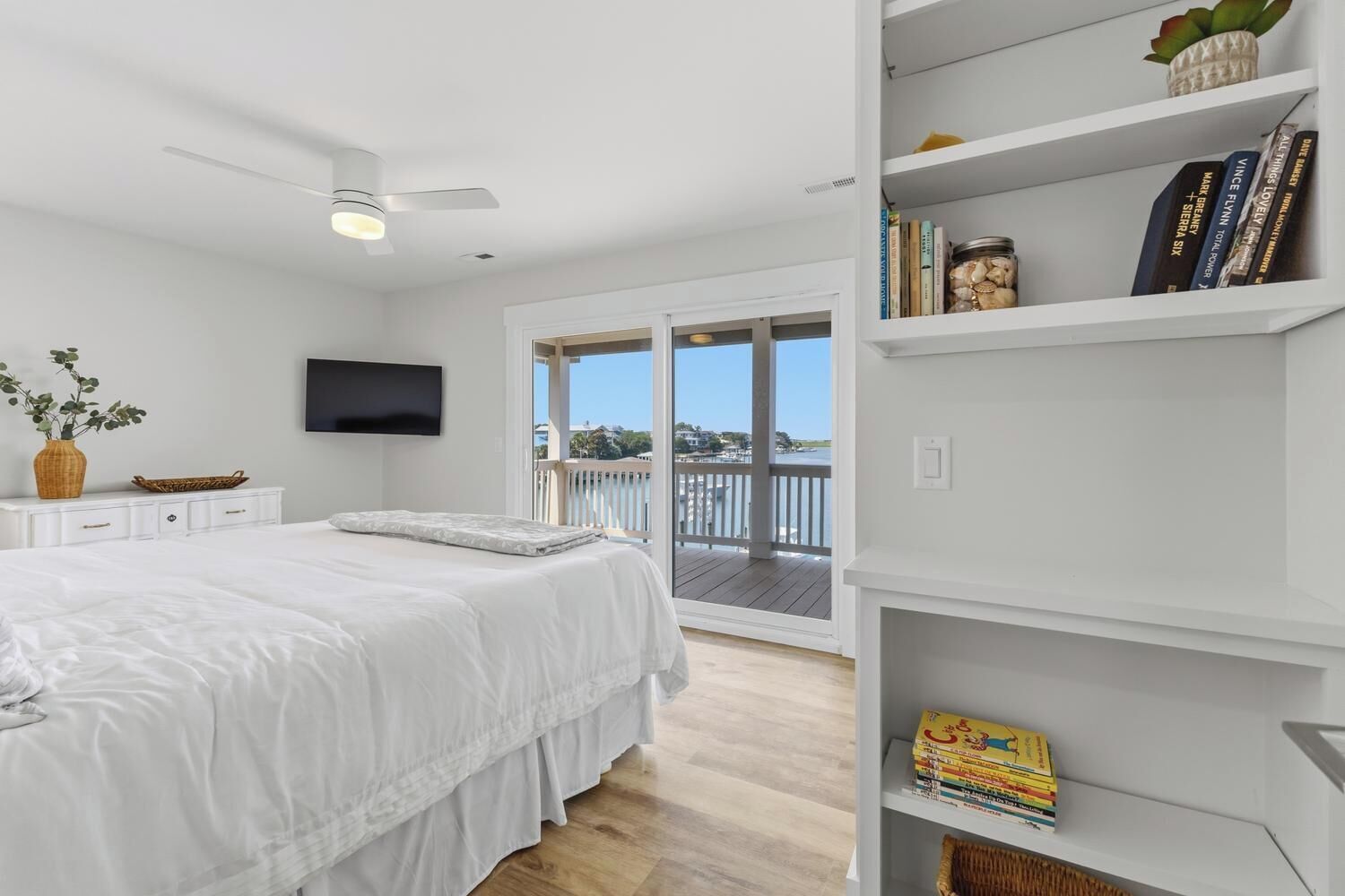 A bedroom with a bed, a television, a bookshelf, and a balcony with a view.