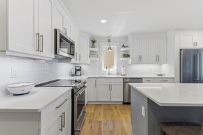 A modern kitchen with white cabinetry, stainless steel appliances, and a wooden floor.
