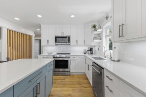 A modern kitchen with white cabinetry, stainless steel appliances, and a wooden floor.