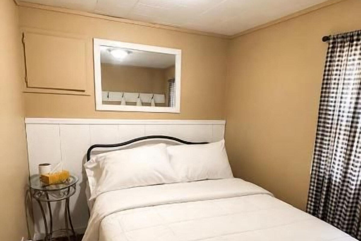 Un lit simple avec une tête de lit, une table de chevet avec une lampe et un miroir au mur.