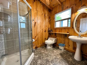 Une salle de bain rustique, aménagée dans une cabane en bois, avec douche, toilettes et lavabo.