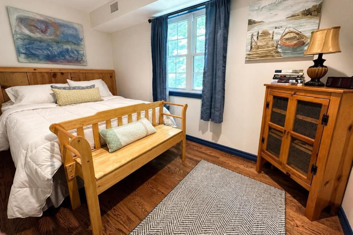 A bedroom with a wooden bed, a bench, a cabinet, and artwork on the walls.