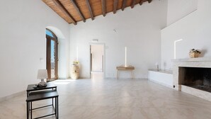 Un'ampia stanza con pavimento in marmo, un camino, un tavolo con una lampada e una porta che dà su un'altra zona.