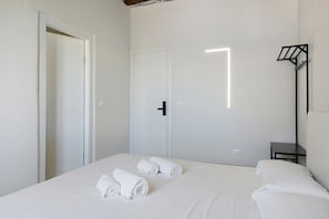 Habitació d'hotel amb un llit, dues tovalloles enrotllades, una tauleta de nit i una làmpada fixada a la paret.