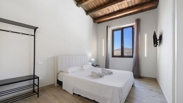 Una camera da letto con un letto, un comodino, una lampada, una finestra e un soffitto in legno.