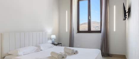 Habitación de hotel con una cama grande, una mesita de noche con lámpara y una ventana con vistas al desierto.