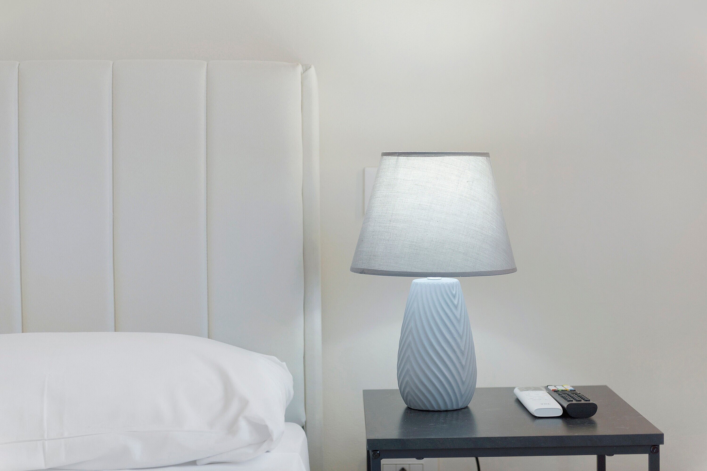 Habitació d'hotel amb un llit, una tauleta de nit amb una làmpada i un comandament a distància.