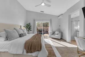 A bedroom with a bed, a bedside table, a chair, and a view of the outdoors. - Early Check-In. AC Comfort + Pool, Spa +FAST WIFI (Coachella)