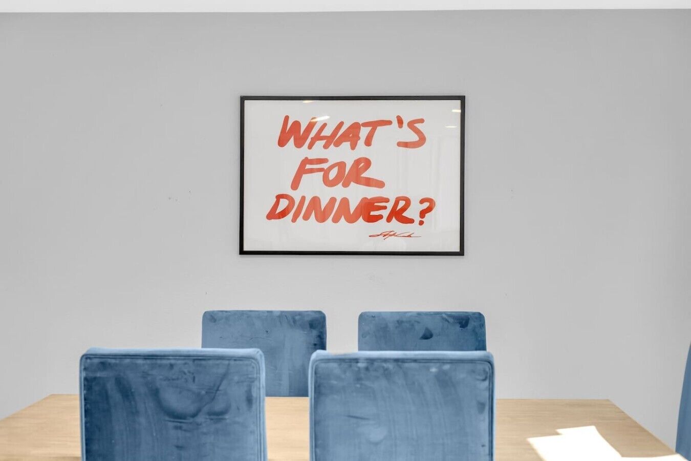 A framed poster with the text 'WHAT'S FOR DINNER?' on a wall above a table with four chairs.