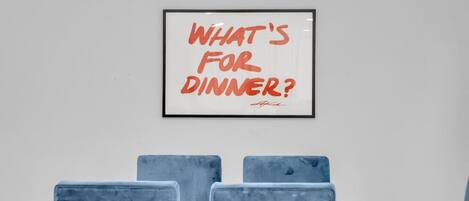 Een lijst met de tekst 'WHAT'S FOR DINNER?' hangt aan de muur boven een tafel met vier stoelen.